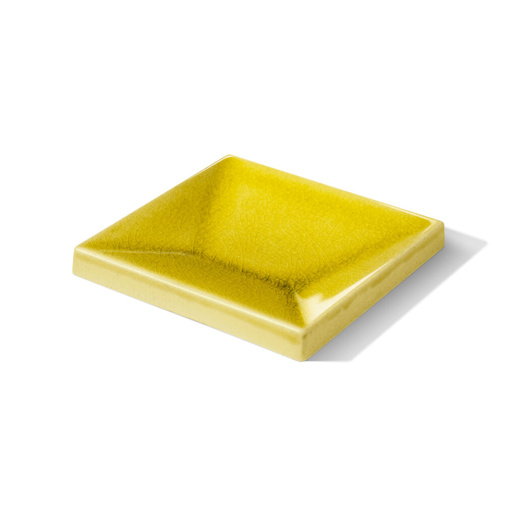 Fliese ESPLANADE konkav in der Farbe Gelb Craquelé. Das Bild zeigt eine einzelne ESPLANADE-Fliese konkav in einem gelben Farbton. Die Datei ist ein Foto im JPEG-Format.